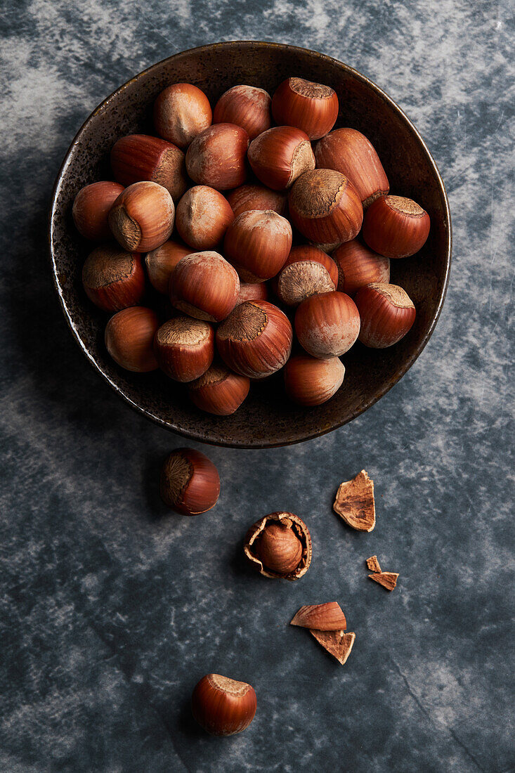 From above bunch of ripe hazelnuts in bowl and shells on marble table