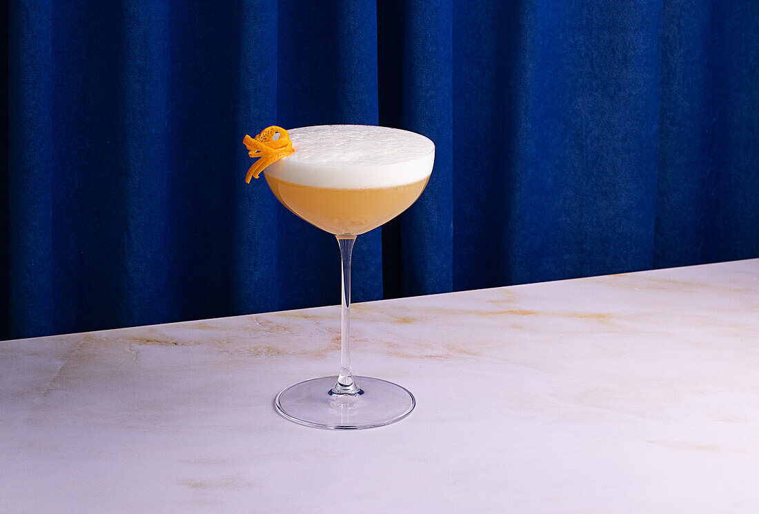 Whiskey-Sour-Cocktail im Glas auf buntem blauem Vorhanghintergrund im Studio
