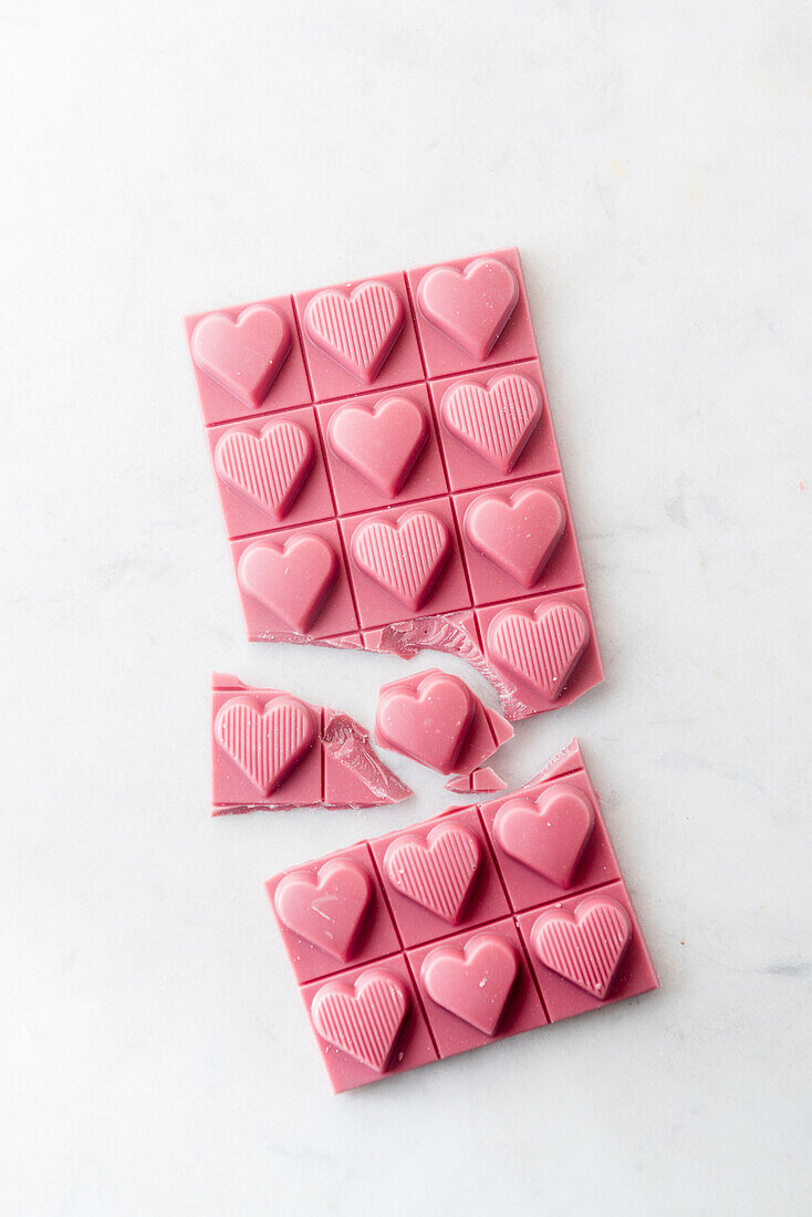 Top view minimalistic composition with pieces of handmade pink chocolate bar with heart shaped design on white background