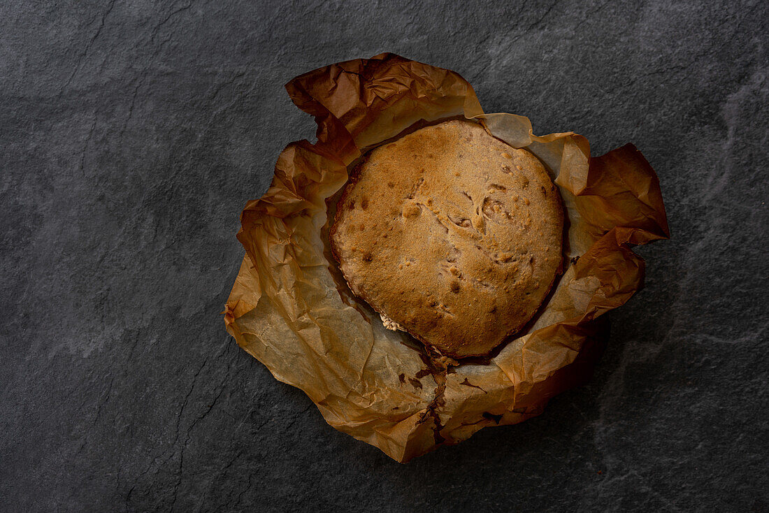 Top view of freshly baked artisan round shaped bread with crispy crust on parchment paper placed on black background
