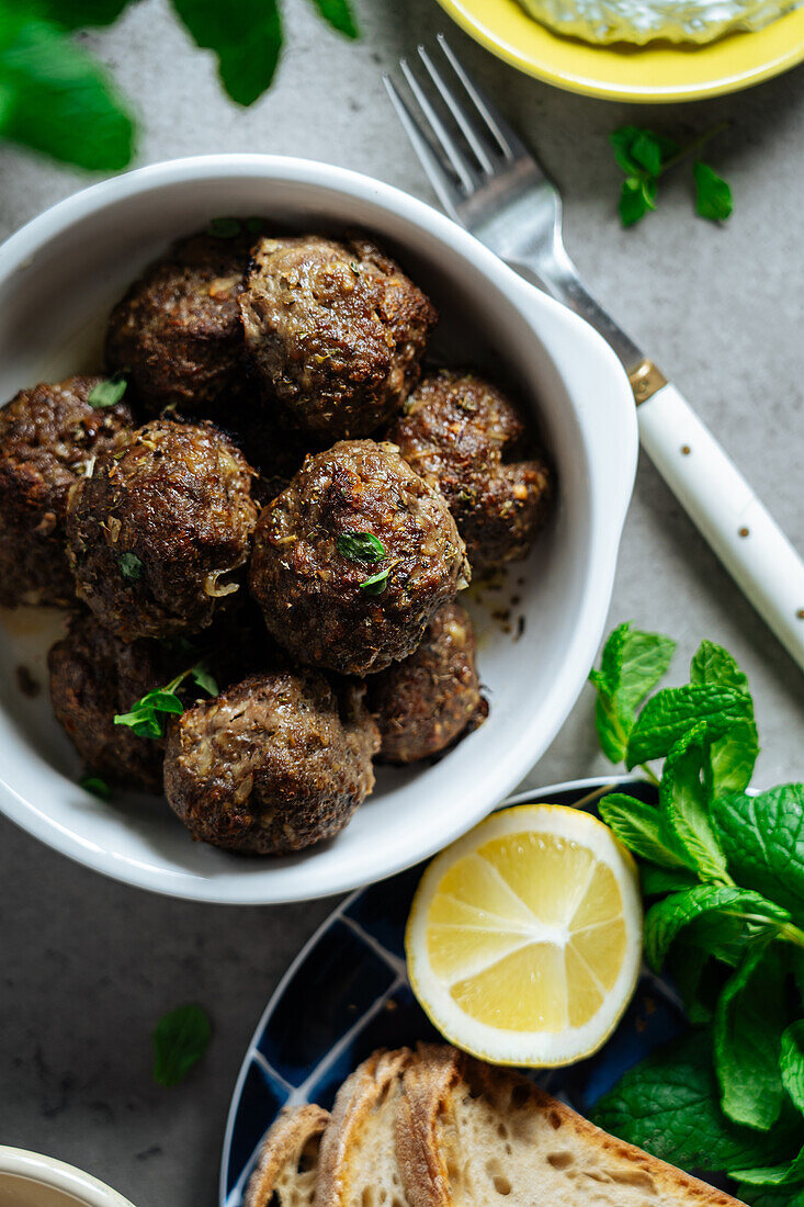 Top view of appetizing traditional homemade fried Greek meatballs served on gray background near plate with bread and lemon in kitchen