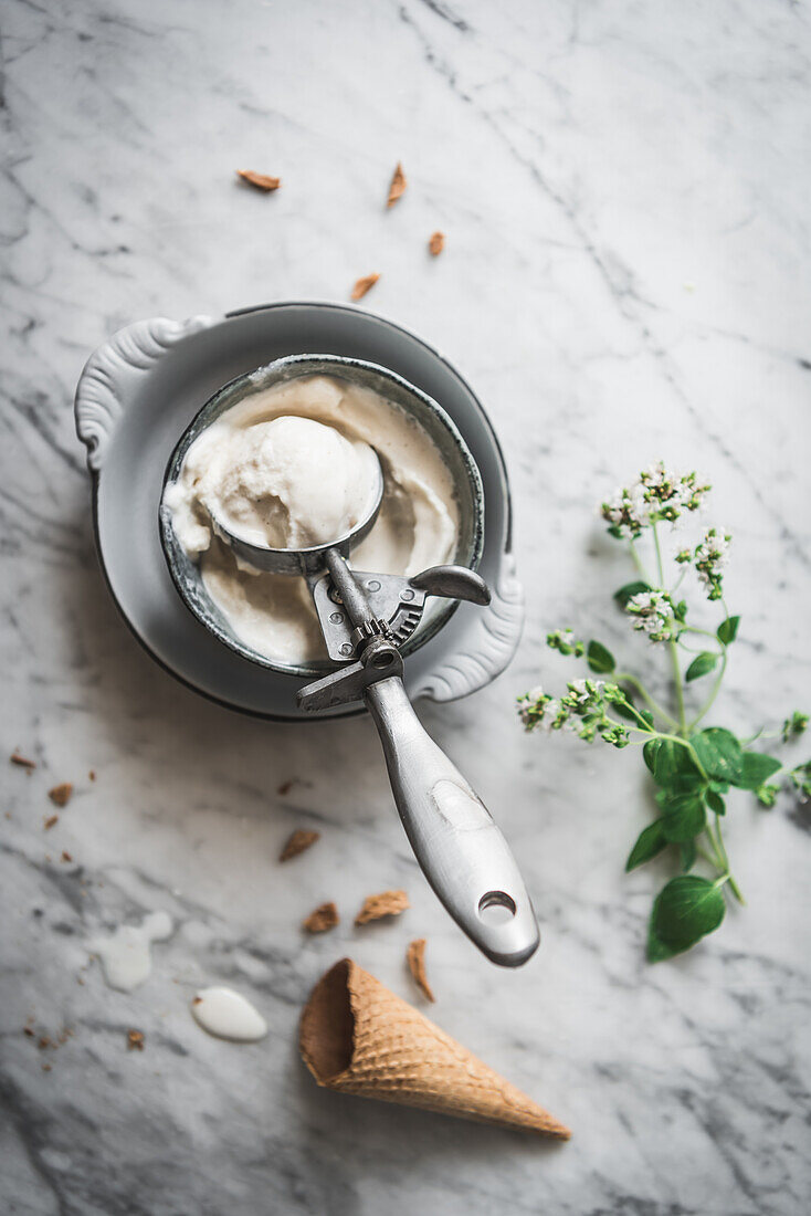 Waffeltüte von oben neben Baisermilch-Gelatokugeln und frischen Minzblättern auf einem Marmortisch