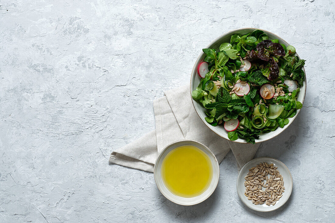 Blick von oben auf einen frischen, gesunden Gemüsesalat in einer Schüssel auf dem Tisch mit Olivenöl und Sonnenblumenkernen