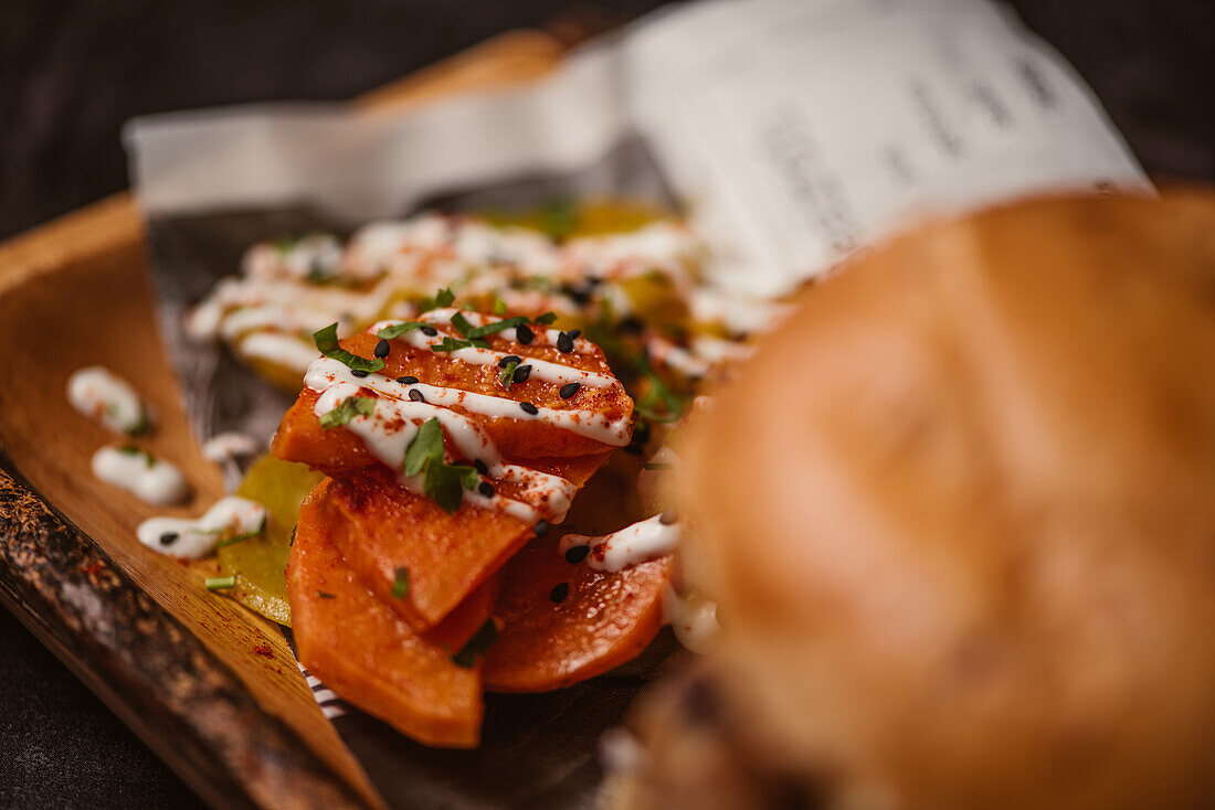 Close up of yummy burger with vegetarian patty and grilled shiitakes between buns near sweet potato and carrot slices with alioli sauce on dark background