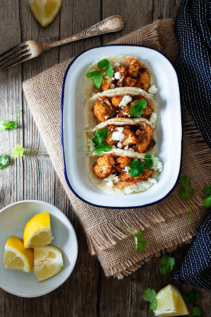 Von oben Blumenkohl-Snack-Tacos in Schüssel und Zitronenstücke in Teller auf Holztisch