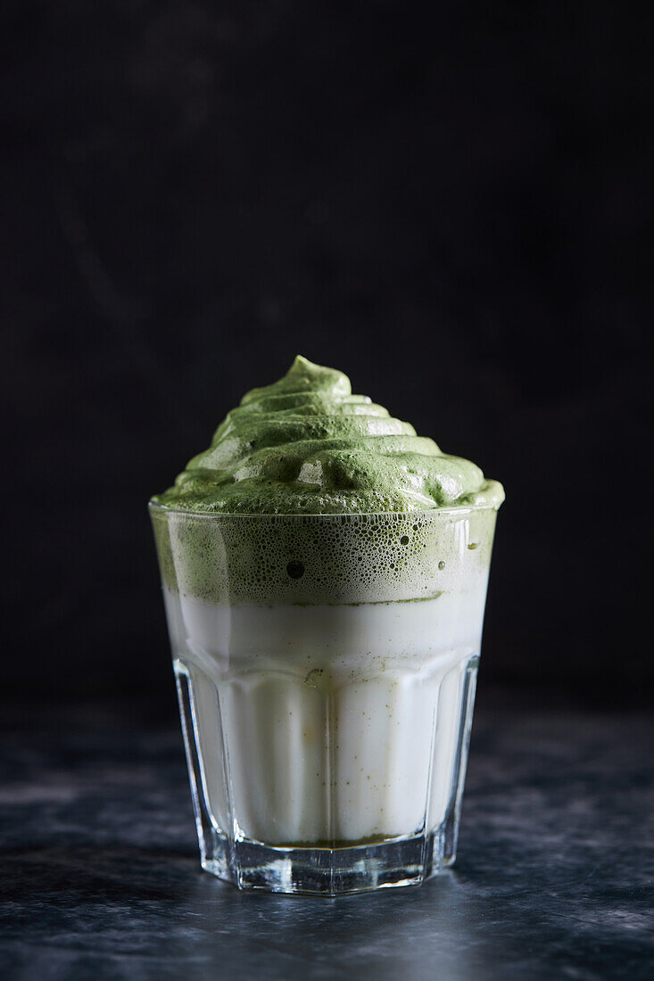 Glas frischer dalgona-Kaffee mit Matcha auf grauer Oberfläche