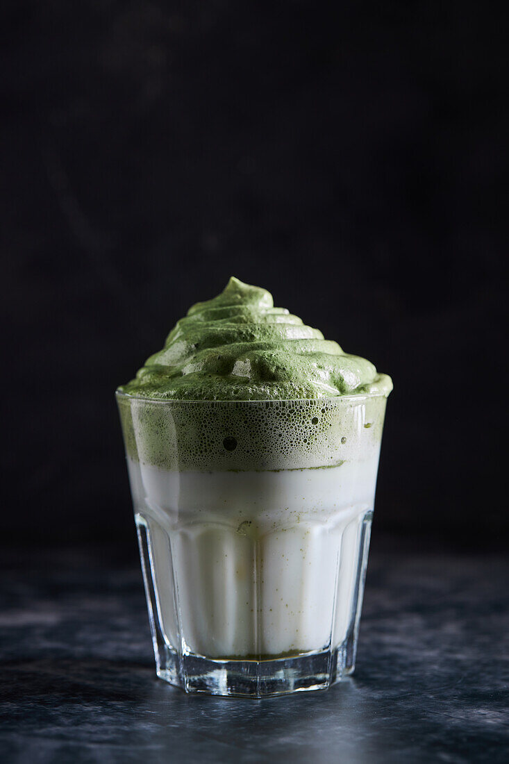 Glass of fresh dalgona coffee with matcha placed on gray surface