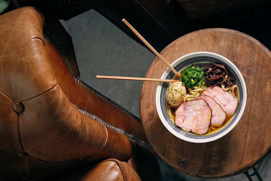 Draufsicht auf eine köstliche traditionelle Ramen-Suppe in einer Schale mit Stäbchen, serviert auf einem runden Tisch