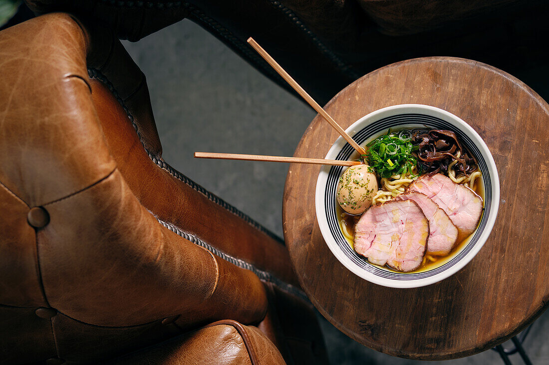 Top view of delicious traditional ramen soup in bowl with chopsticks served on round table