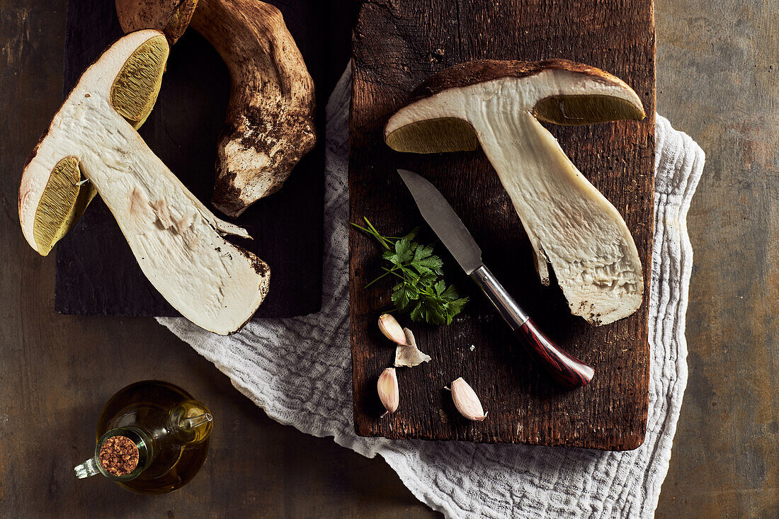 Top view of raw cut Boletus edulis mushrooms on wooden chopping board with garlic and parsley in light kitchen during cooking process