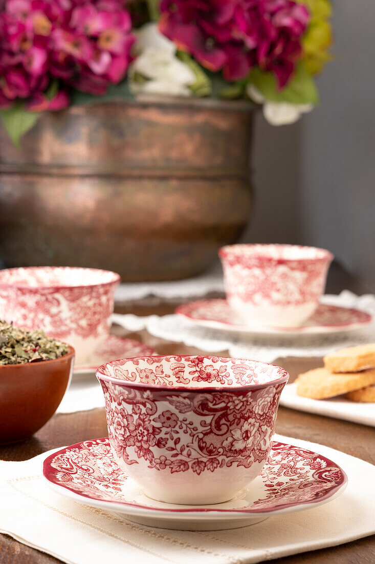 Ornamentale Keramiktassen auf einem Tisch mit Blumen für die Teestunde in einem gemütlichen Zimmer zu Hause