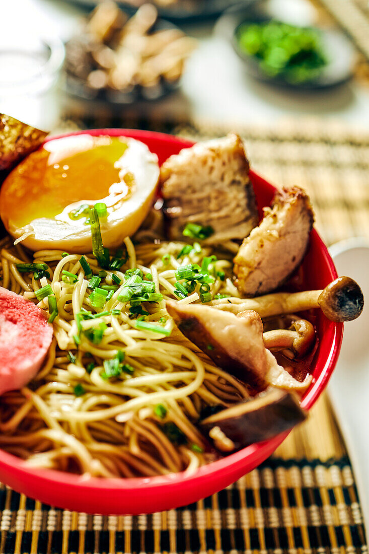 Von oben auf appetitliche Ramen-Suppe mit Fleisch und Ei und Nudeln, serviert in einer Schüssel auf einem Tisch neben Stäbchen und einer Glastasse