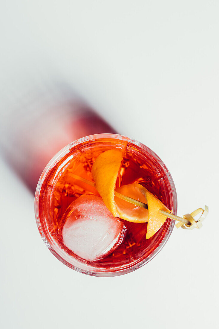 Glas mit bitterem alkoholischem Negroni-Cocktail, serviert mit Eis und Orangenschale auf weißer Fläche