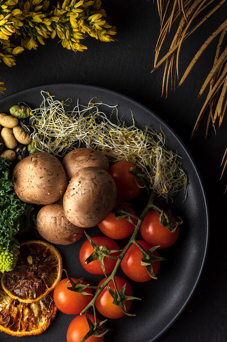 Top view of plate with bundle of fresh cherry tomatoes near cooked potatoes and sprouts on gray background with flowers