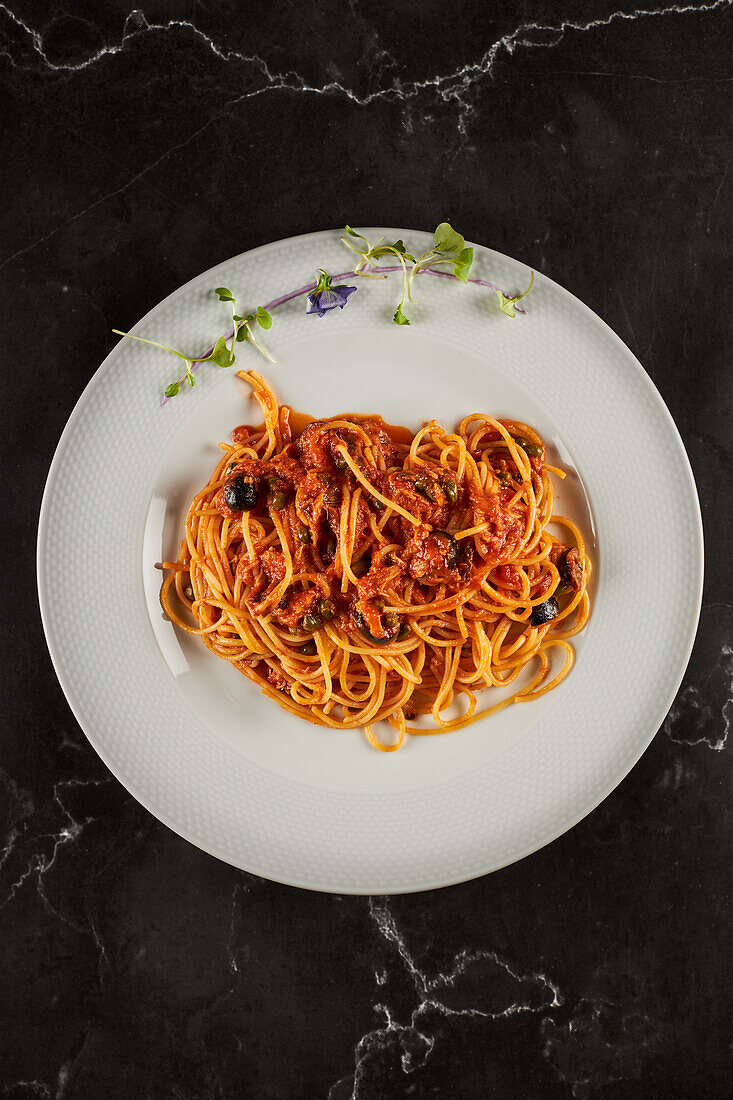 Draufsicht auf leckere Spaghetti alla puttanesca mit Tomatensoße und Meeresfrüchten, garniert mit Knoblauch und Chilischoten, serviert auf einem Teller in einem italienischen Restaurant