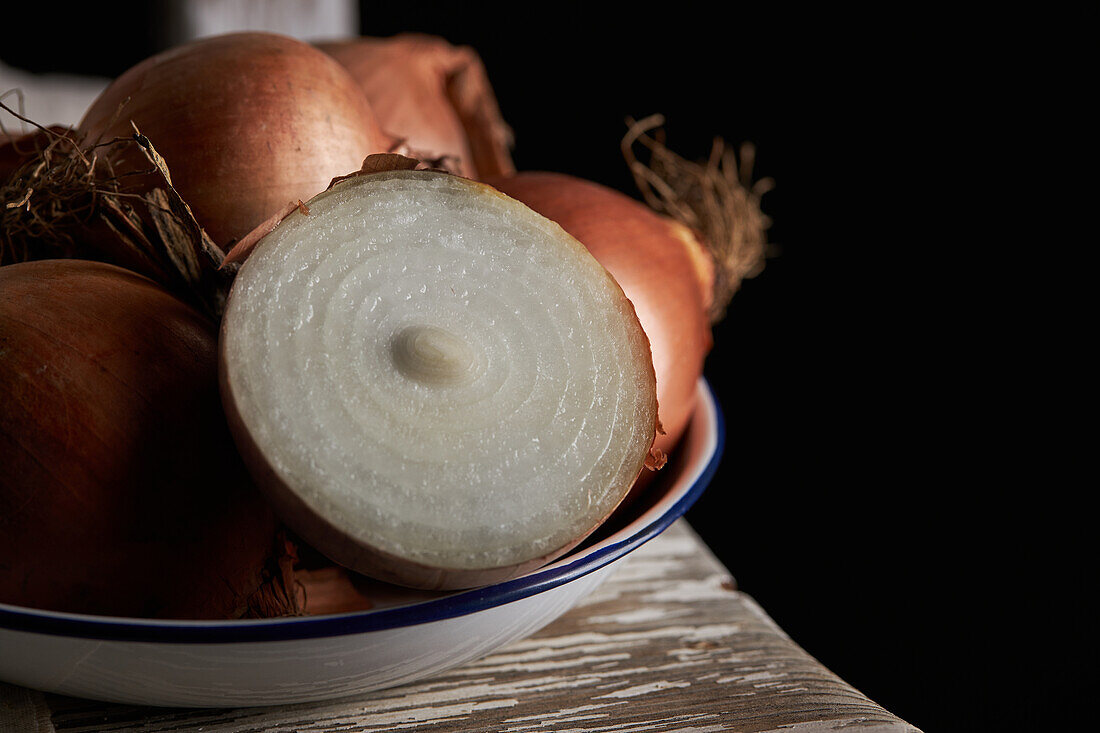 Closeup halved and whole unpeeled onions placed in bowl on shabby chair on black background
