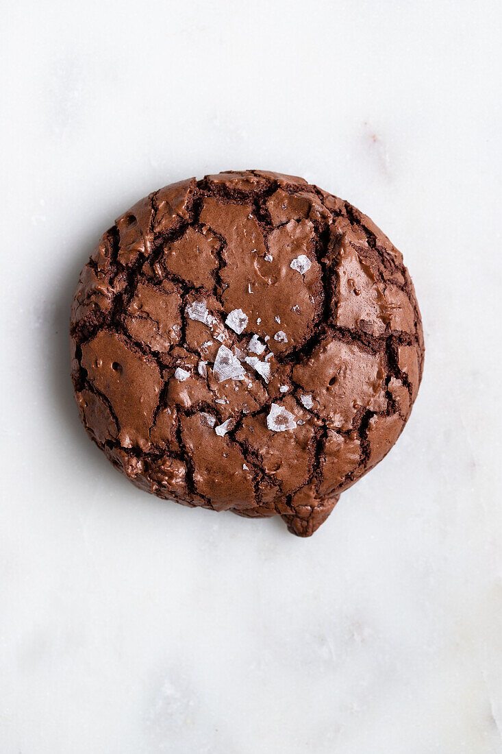 Top view of sweet freshly baked chocolate brownie cookie with cracks placed on white background in light kitchen at home