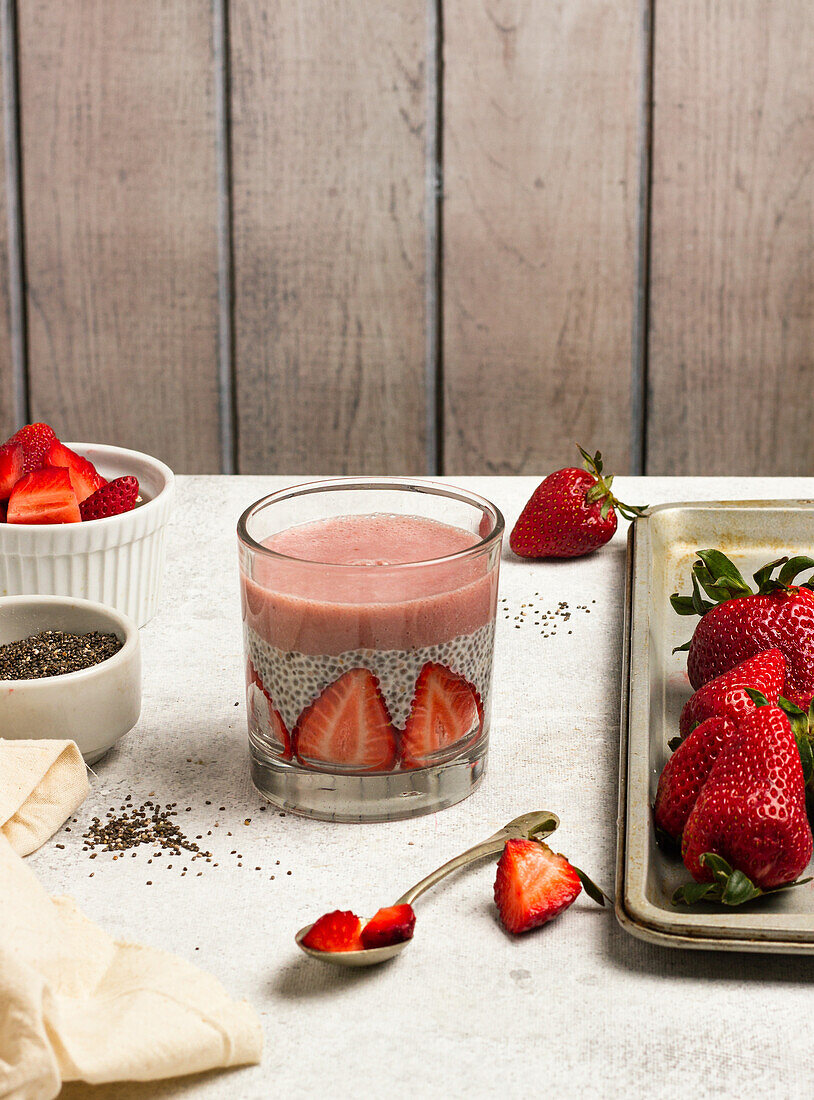 Leckerer Pudding mit Chiasamen und Scheiben von frischen Erdbeeren auf dem Tisch neben den Zutaten für ein gesundes Frühstück