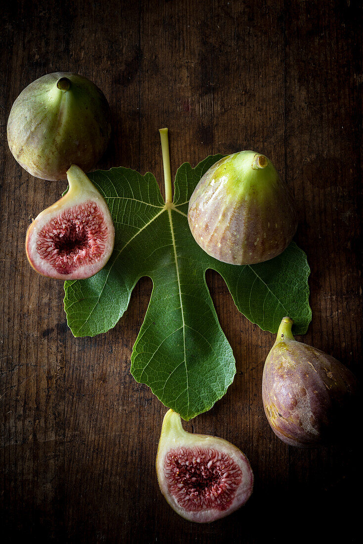Top view of ripe halved and whole figs placed with green leaf on wooden rustic table