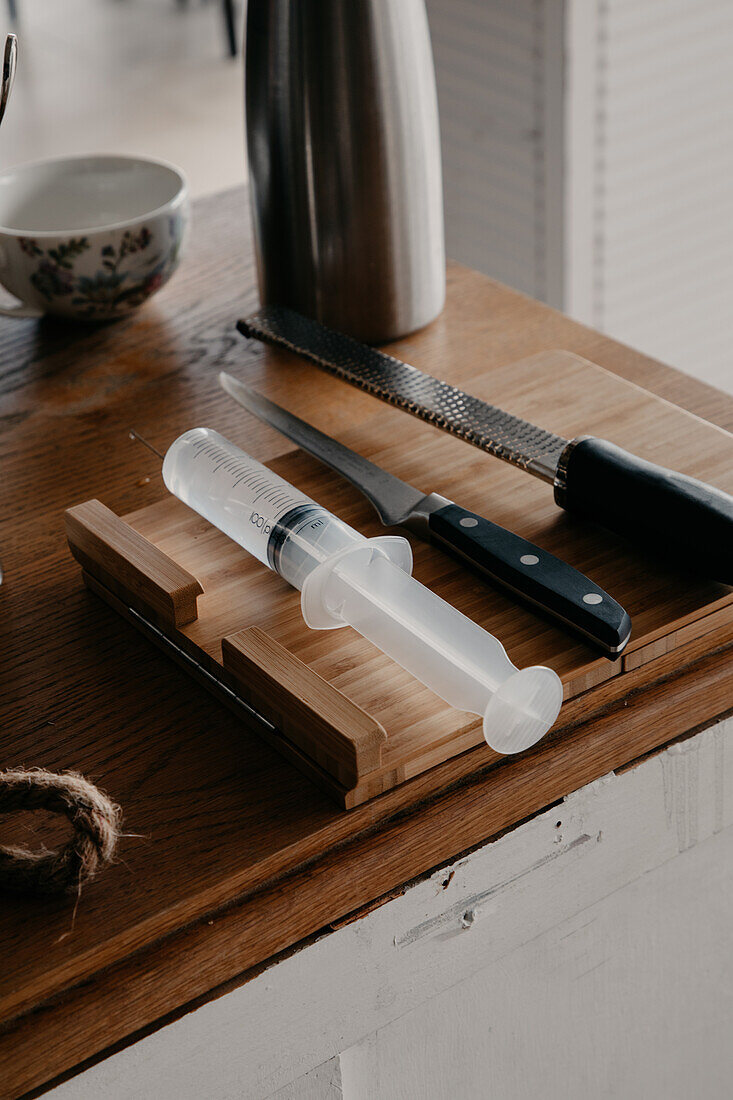 From above of various sharp knives and culinary syringe placed on wooden cutting board in kitchen