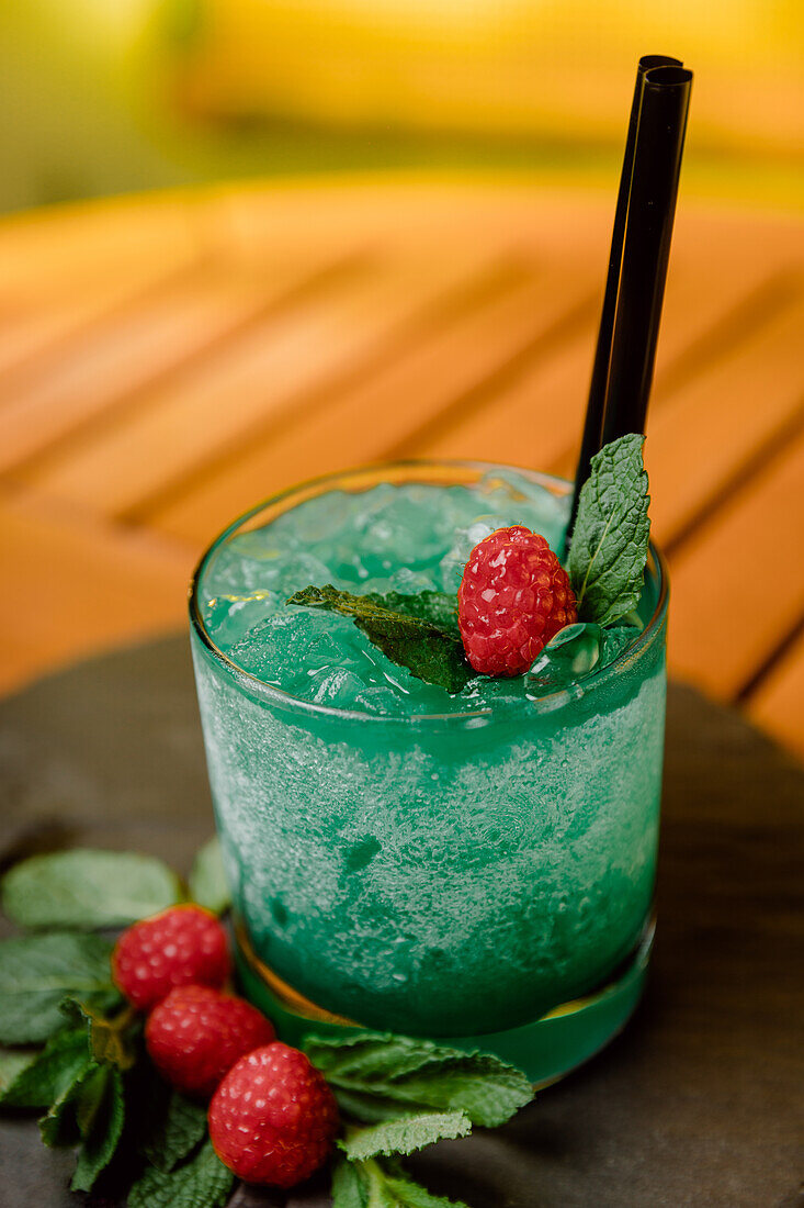 High angle of exotic cocktail made of gin with passion fruit mixed with lemon juice and blue curacao served with berry and mint leaves