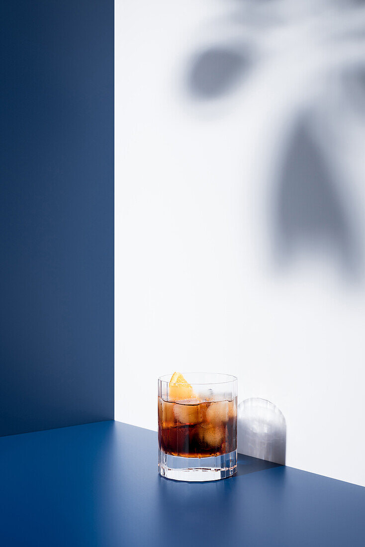 Glas alkoholischer Cocktail mit rotem Wermut, serviert mit Orangenscheiben in einem hellen Studio mit blauer und weißer Wand