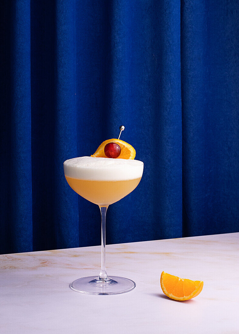 Whiskey sour cocktail in glass on colorful blue curtain background in studio