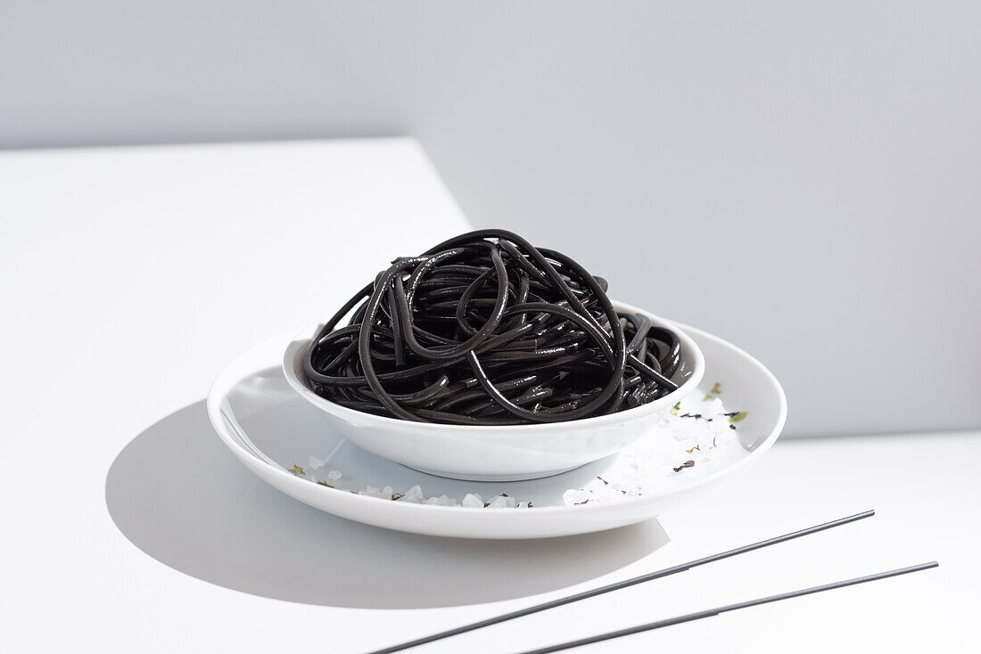 Von oben auf Keramikschale mit leckeren Spaghetti mit schwarzer Tintenfischtinte mit Stäbchen auf grauem Hintergrund