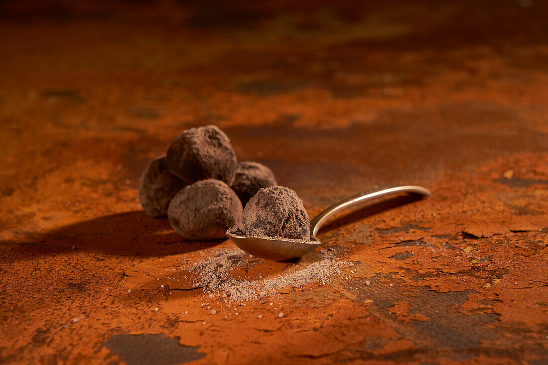 From above of composition on small metal spoon with delicious delectable chocolate truffles and cocoa powder placed on rusty surface