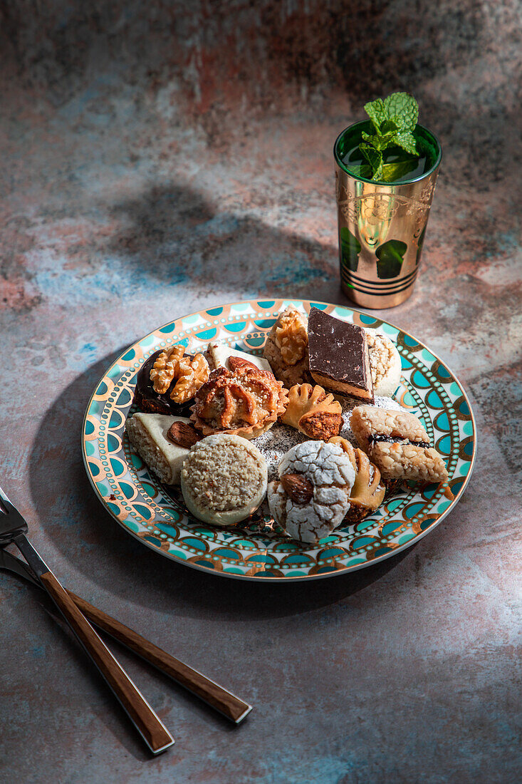 Von oben Baklava und Kekse mit marokkanischem Pfefferminztee neben Messer und Gabel auf einem mit Minzblättern dekorierten Tisch
