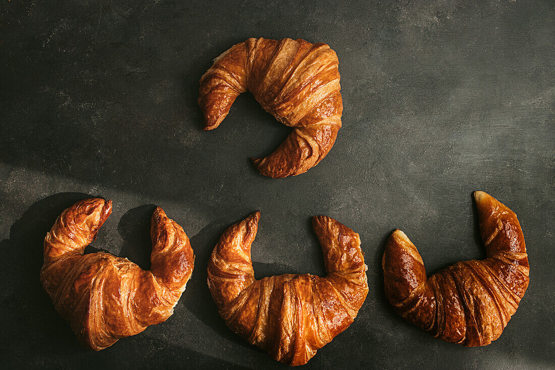 Top view composition with appetizing freshly baked crusty croissants served dark background