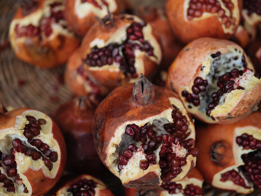 Delicious whole fresh pomegranates with seeds placed on wooden background of bowl in daylight