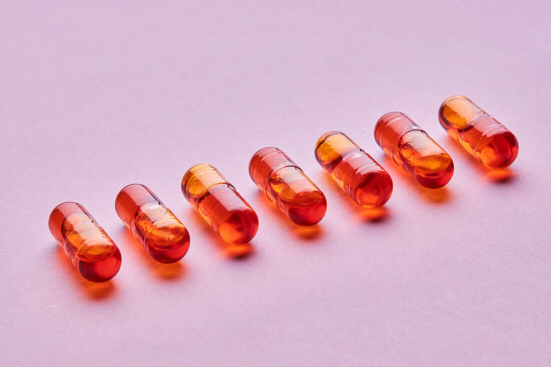 Komposition von orangefarbenen Pillen auf rosa Hintergrund in einem hellen Studio von oben betrachtet