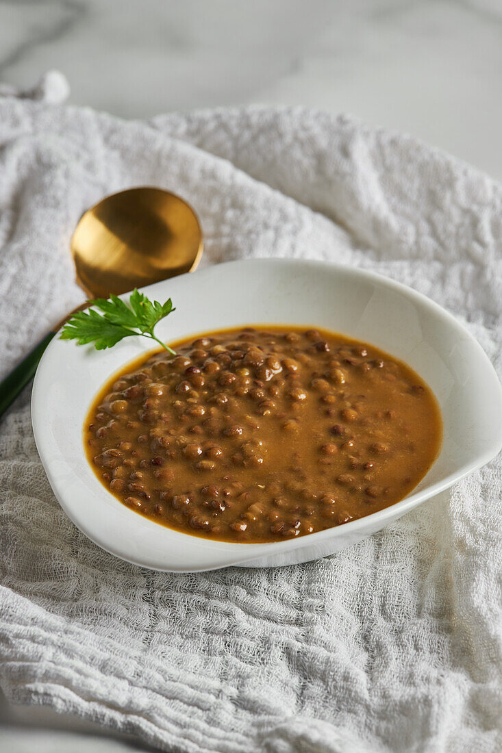 Weiße Schale mit köstlicher Linsensuppe von oben, garniert mit Petersilie, auf einer Serviette neben dem Löffel