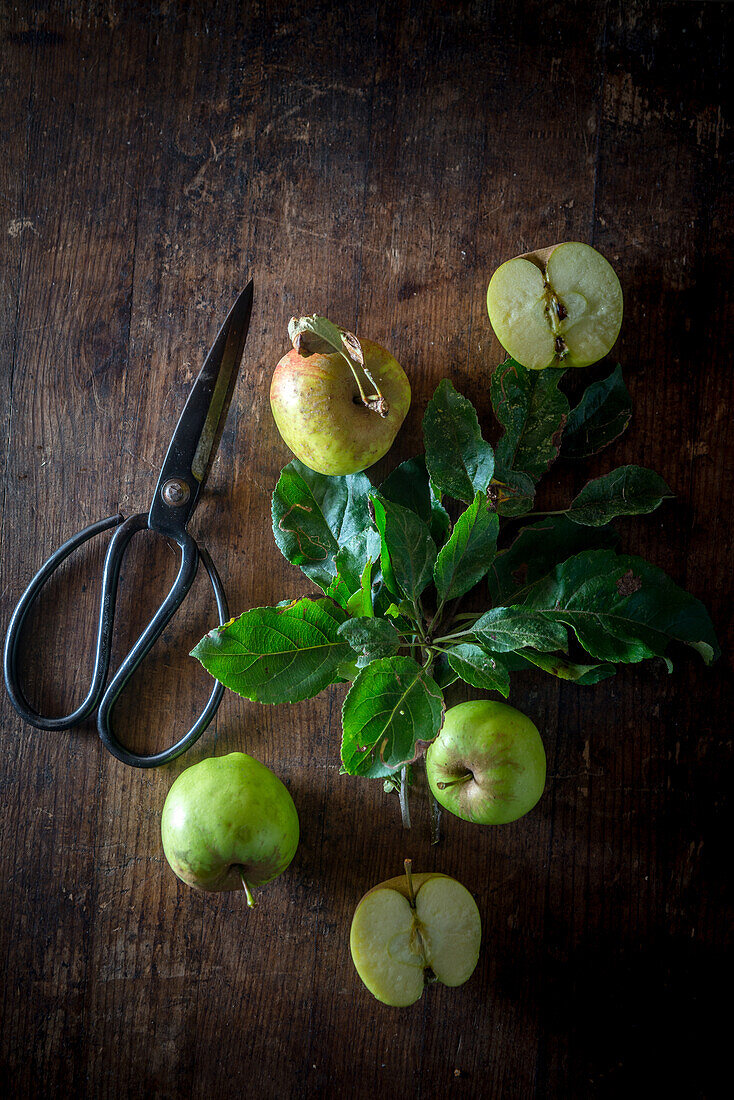 Top view of sweet ripe green apples arranged with leaves on rustic wooden table near scissors