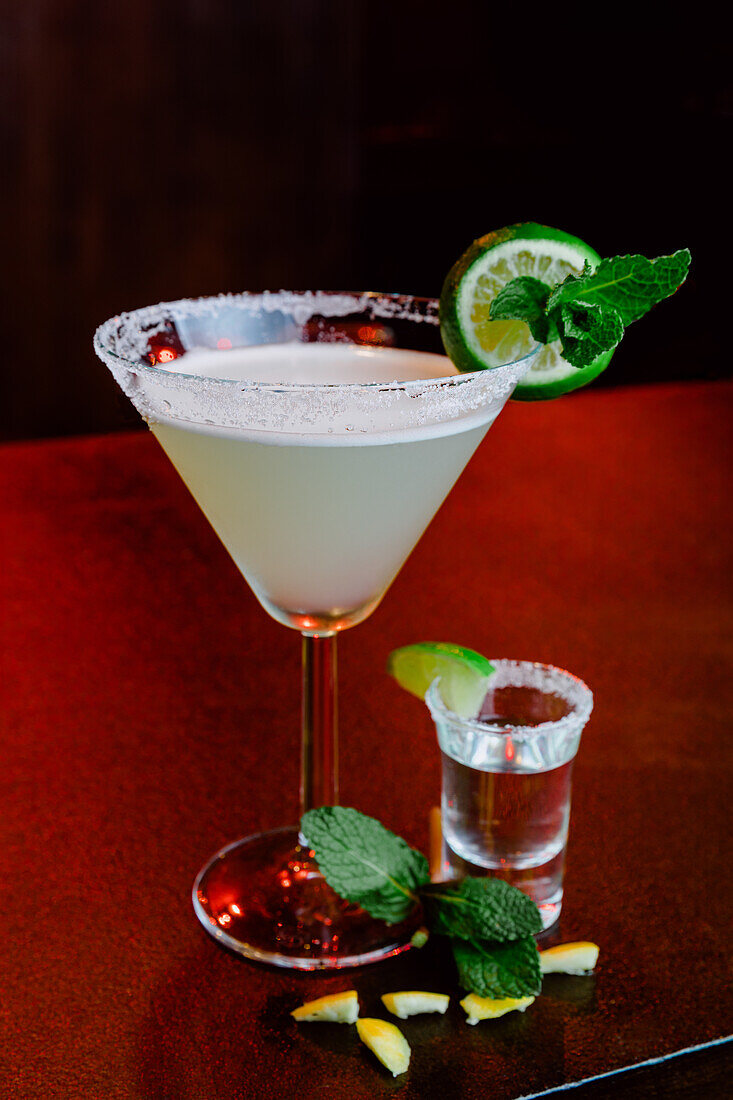 Crystal glass of alcoholic cocktail Margarita consisting of tequila orange liqueur and lime juice served with salt on rim of glass and mint leaf