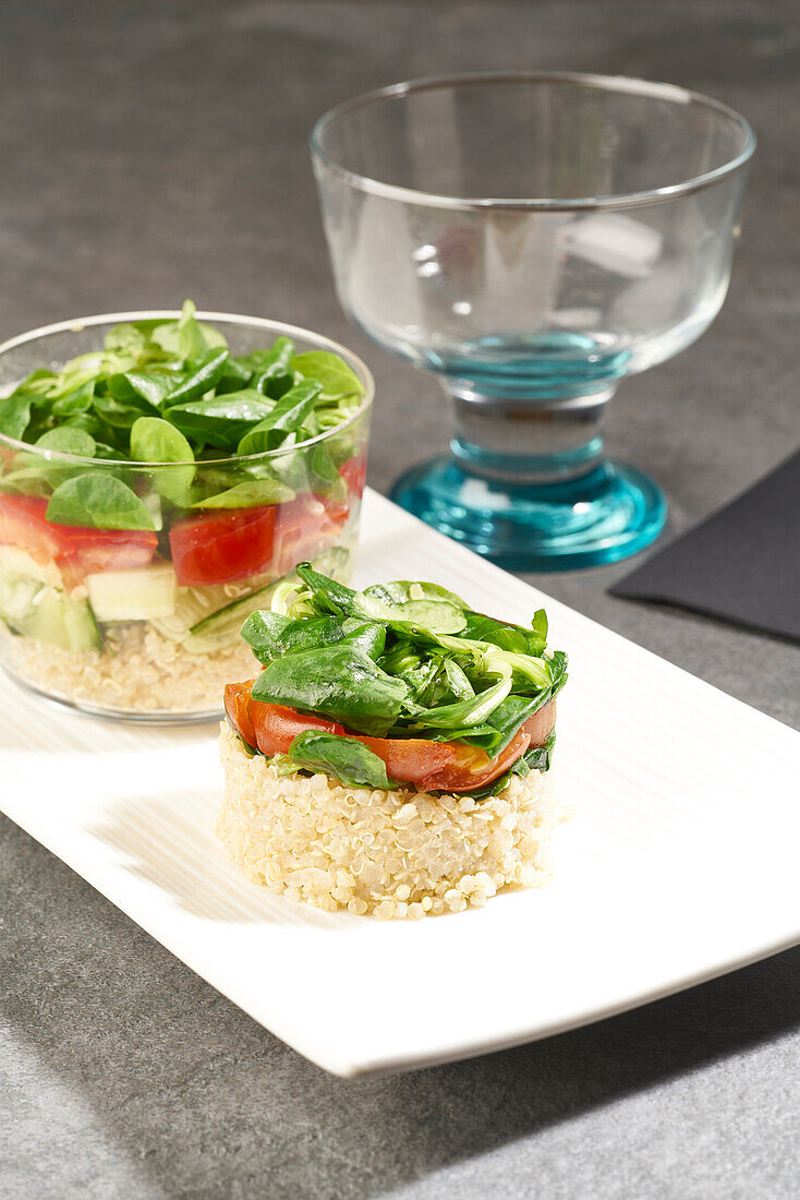 Hoher Winkel von schmackhaftem Salat aus Reis und Gemüse in runder Form und im Glas serviert auf weißem Teller auf grauem Tisch