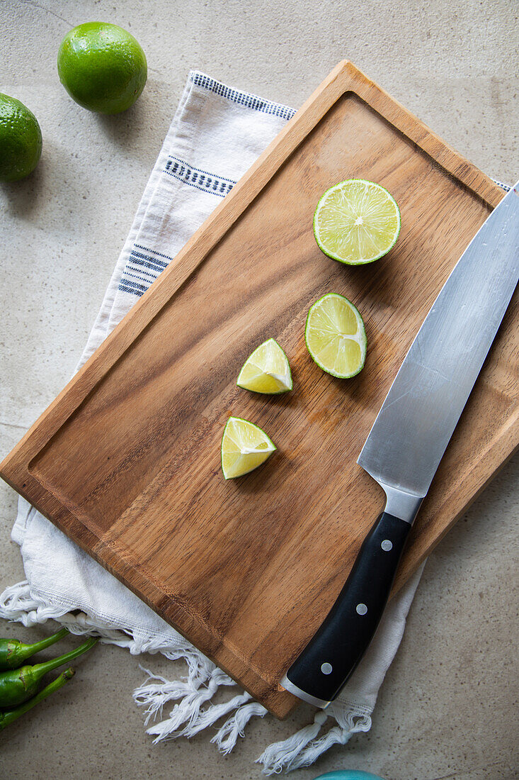 Draufsicht auf eine geschnittene frische grüne saure Limette auf einem hölzernen Schneidebrett mit einem scharfen Messer auf einem Tisch in einer hellen Küche
