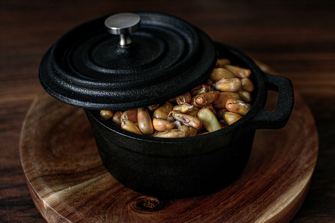 High angle of heap of cereal grain in black saucepan with lid placed on wooden board on table in kitchen