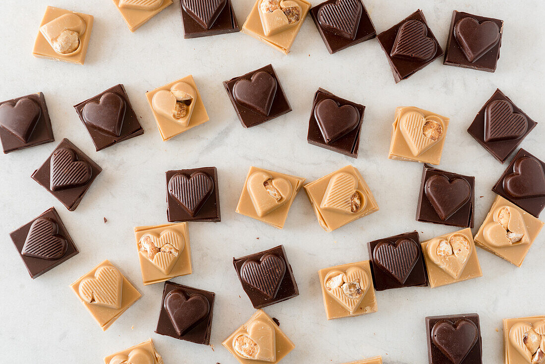 Draufsicht auf leckere Schokoladenbonbons mit Nüssen in Herzform auf weißem Hintergrund verstreut