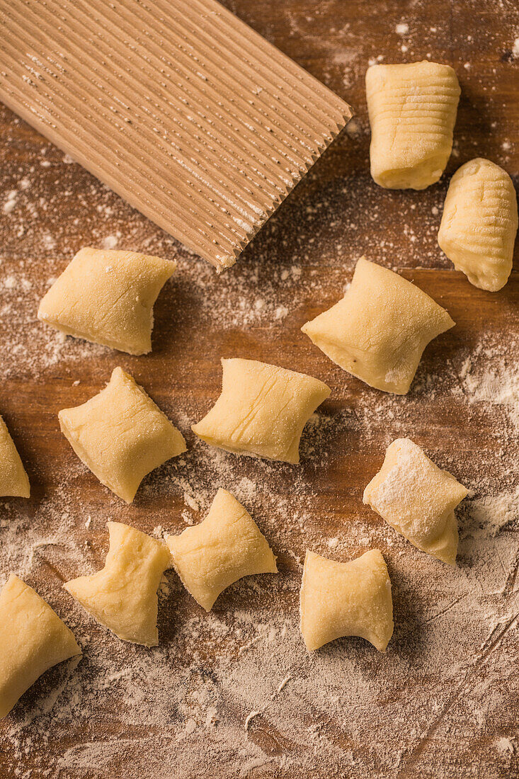 Top view of pieces of soft raw dough placed on wooden table covered with flour near ribber board during gnocchi preparation in the kitchen