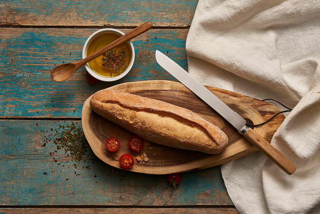 Top view of homemade baguette bread on wooden cutting board with cherry tomatoes and knife on shabby table
