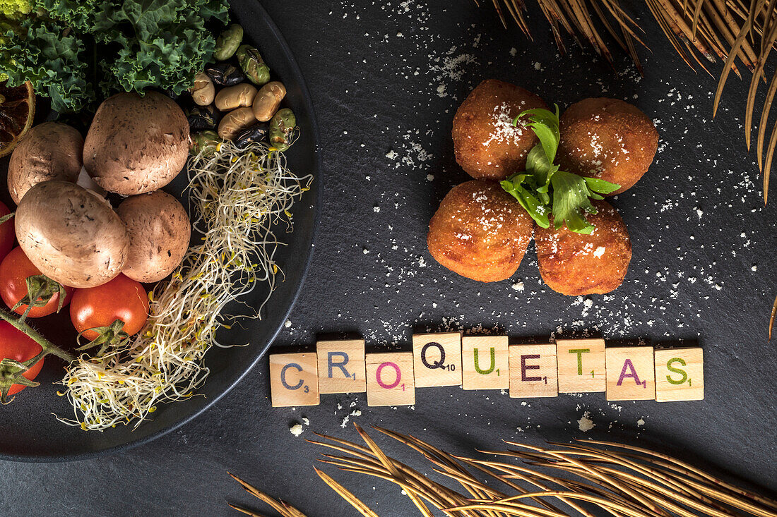 Overhead view of decorative title under deep fried croquettes and plate with healthy food on gray background