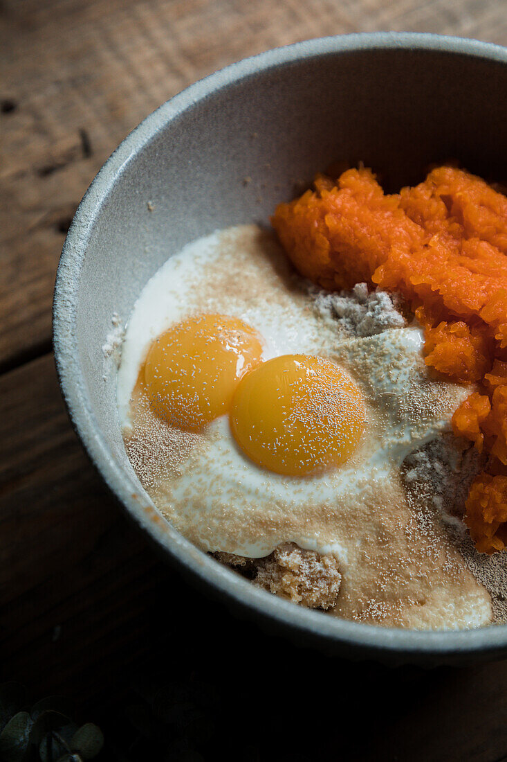 Schüssel mit Kürbispüree, Eiern und Mehl für die Zubereitung von Kuchen auf einem Holztisch
