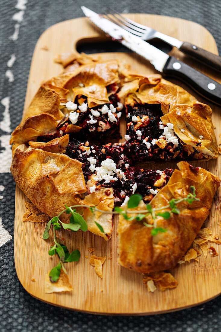 Top view of baked cut pie with beetroot and feta cheese on wooden cutting board with knife on gray background in kitchen