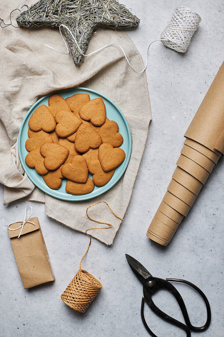 Top view of layout of sweet heart shaped Christmas biscuits on plate and assorted wrapping materials on table