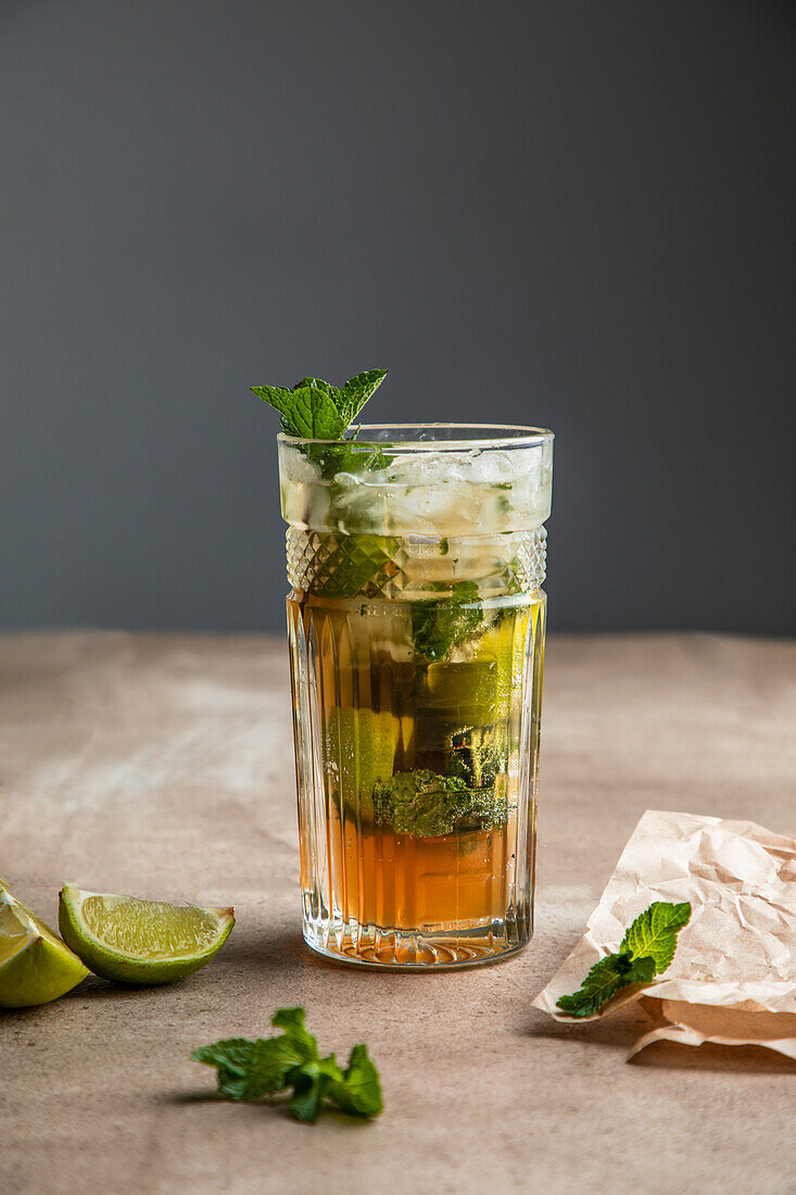 Refreshing cold alcoholic mojito with ice mint leaves and cut lime on wooden board