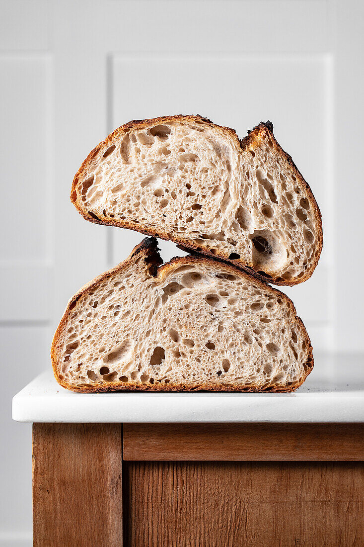 Halves of tasty sourdough bread with brown crust placed on table against white backdrop