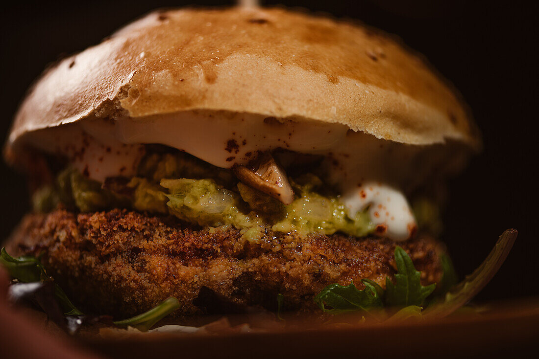 Nahaufnahme eines leckeren Burgers mit vegetarischer Frikadelle und gegrillten Shiitakes zwischen Brötchen neben Süßkartoffel- und Karottenscheiben mit Alioli-Sauce auf dunklem Hintergrund