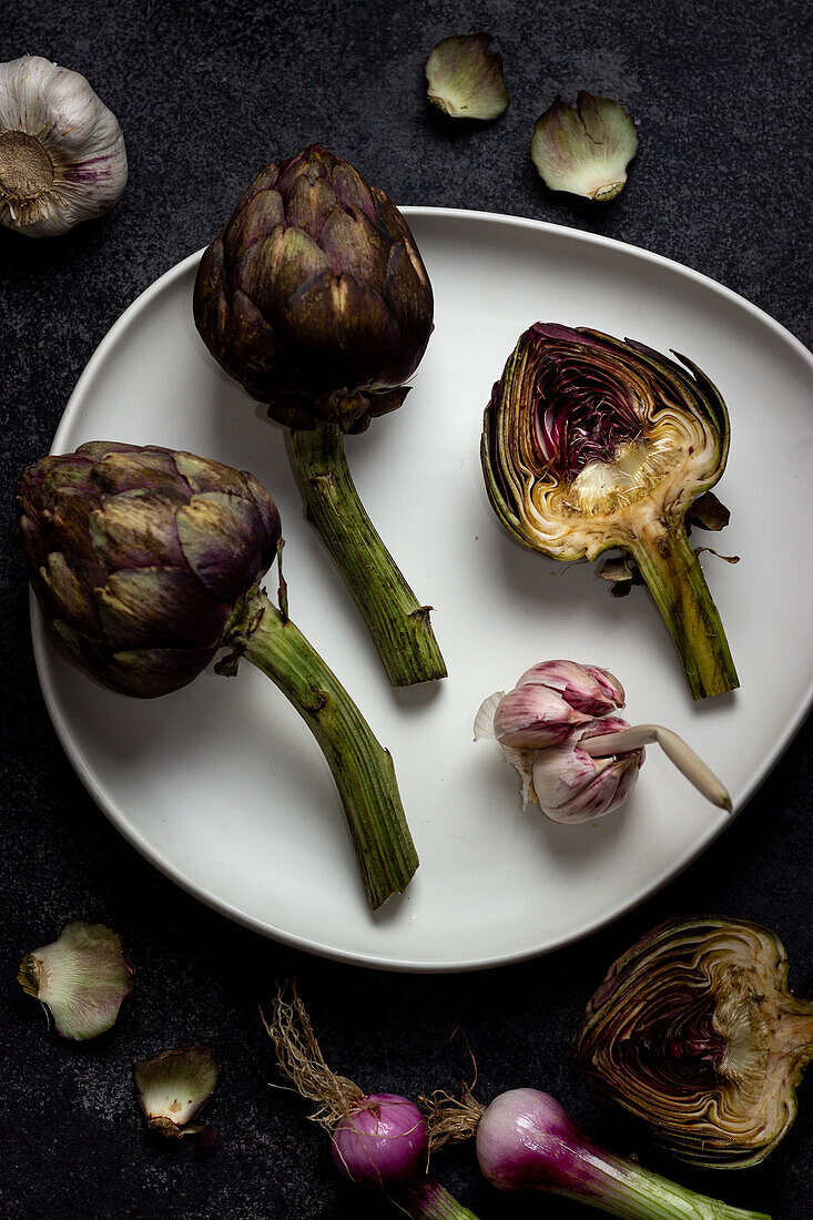 From above ripe green artichokes with garlic on ceramic plate placed on black table background